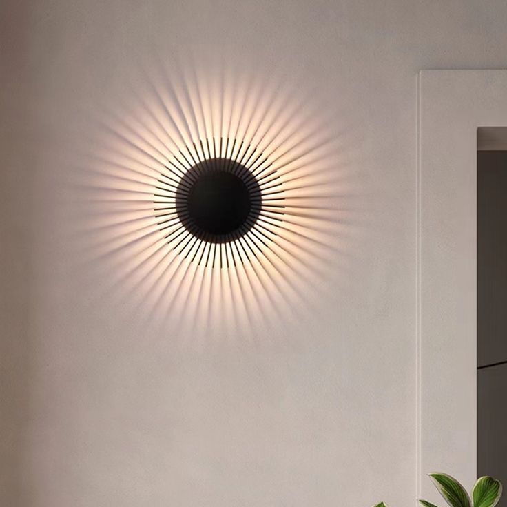 a round light fixture mounted on the wall above a potted plant in a white room