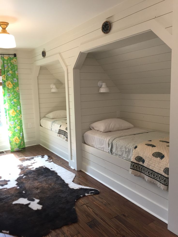 two beds in a room with white walls and wood flooring, one is built into the wall