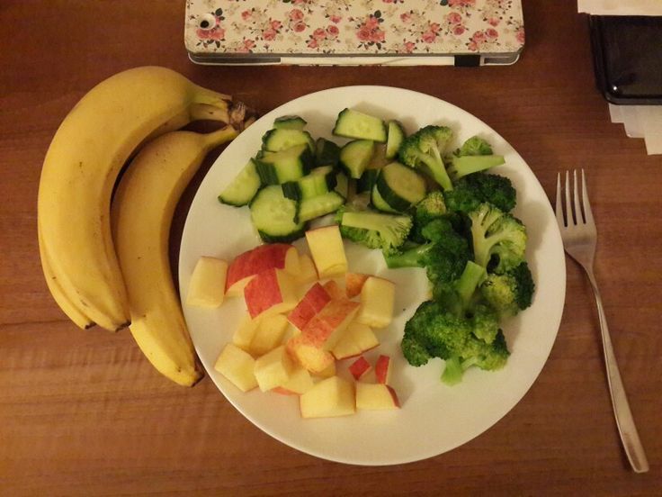 a white plate topped with fruit and vegetables next to a knife and fork on a wooden table