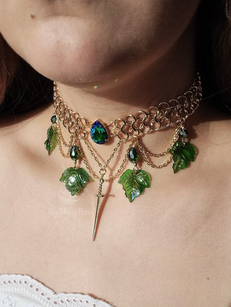 Behold the elegance of this gold-hued chainmail necklace! A vivid green rhinestone steals the spotlight at the heart, while a dangling sword charm and cascading layers of chains adorned with green teardrop beads and delicate ivy leaves add a touch of enchantment. Fit for a fairy warrior queen, this unique statement piece is destined to captivate. Actual colors of any item or chains may slightly differ from screen to screen due to the screen resolution. I take our pictures in natural light during Fairy Warrior, Chainmail Choker, Warrior Necklace, Ethereal Jewelry, Chainmail Necklace, Fantasy Necklace, Ivy Leaves, Chunky Statement Necklace, Warrior Queen