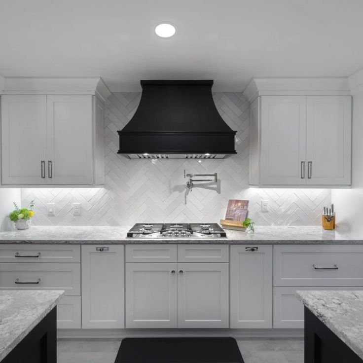 a kitchen with white cabinets and marble counter tops, an oven hood over the stove