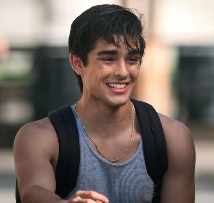 a young man smiles while he walks down the street with his hand in his pocket