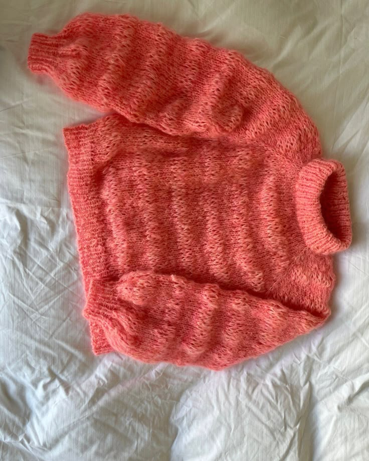 an orange sweater laying on top of a bed