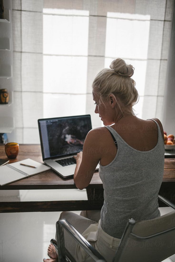 a woman sitting at a desk with a laptop on her lap and looking out the window