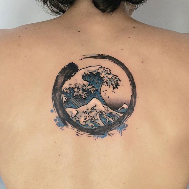 the back of a woman's shoulder with a wave tattoo on her upper arm