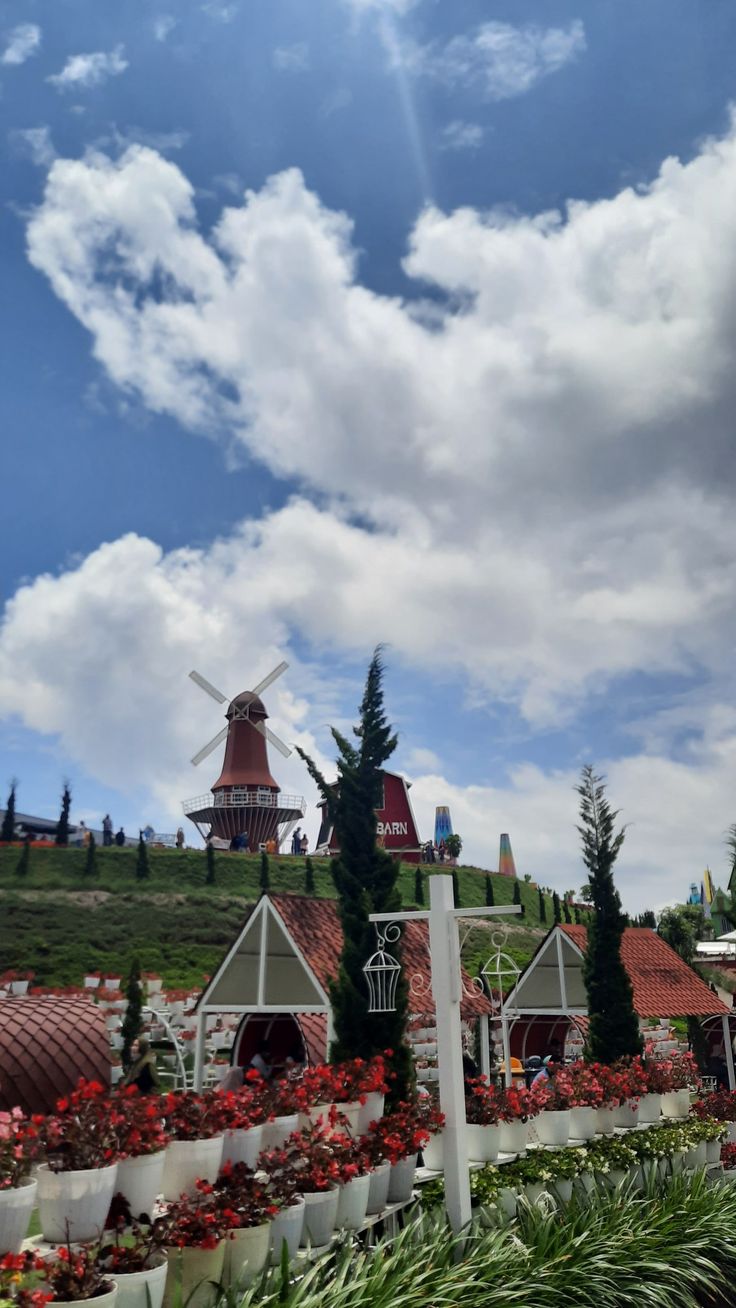 a windmill is in the distance on top of a hill surrounded by flowers and trees