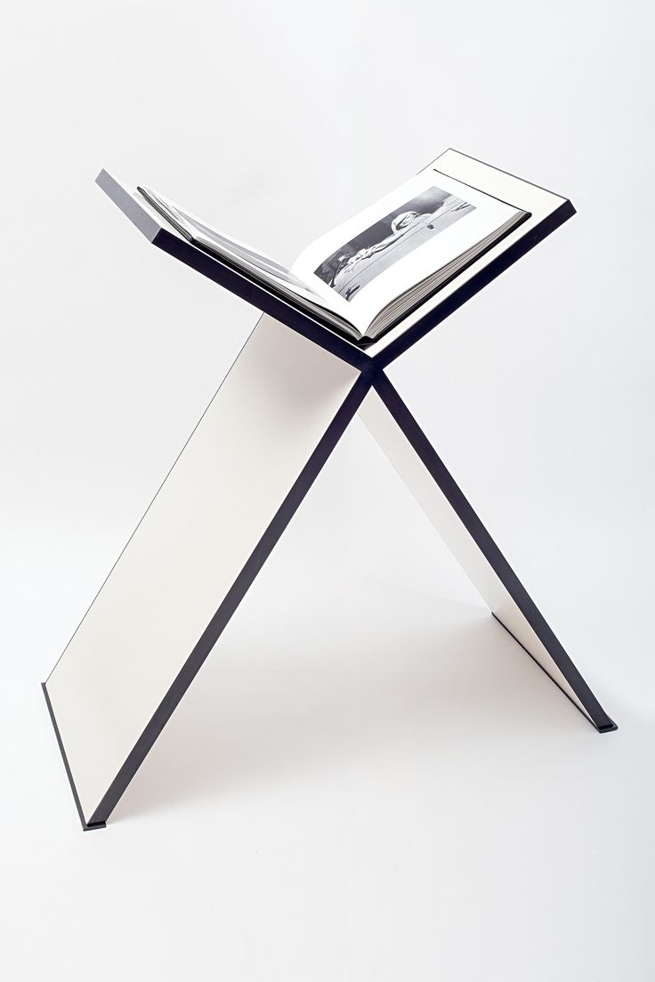 an open book sitting on top of a metal cross legged table with a magazine holder underneath it