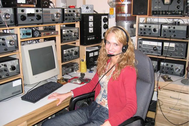 a woman sitting in front of a computer with headphones on and many other electronic equipment behind her