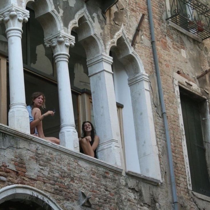 two people are sitting on the balcony of an old building and pointing at something in the distance