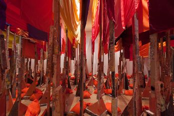 many orange and red flags hanging from poles in a room filled with wooden poles,