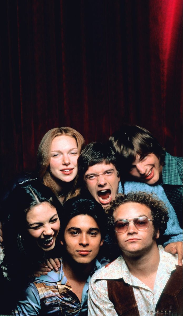 a group of people standing next to each other in front of a red curtain with their mouths open