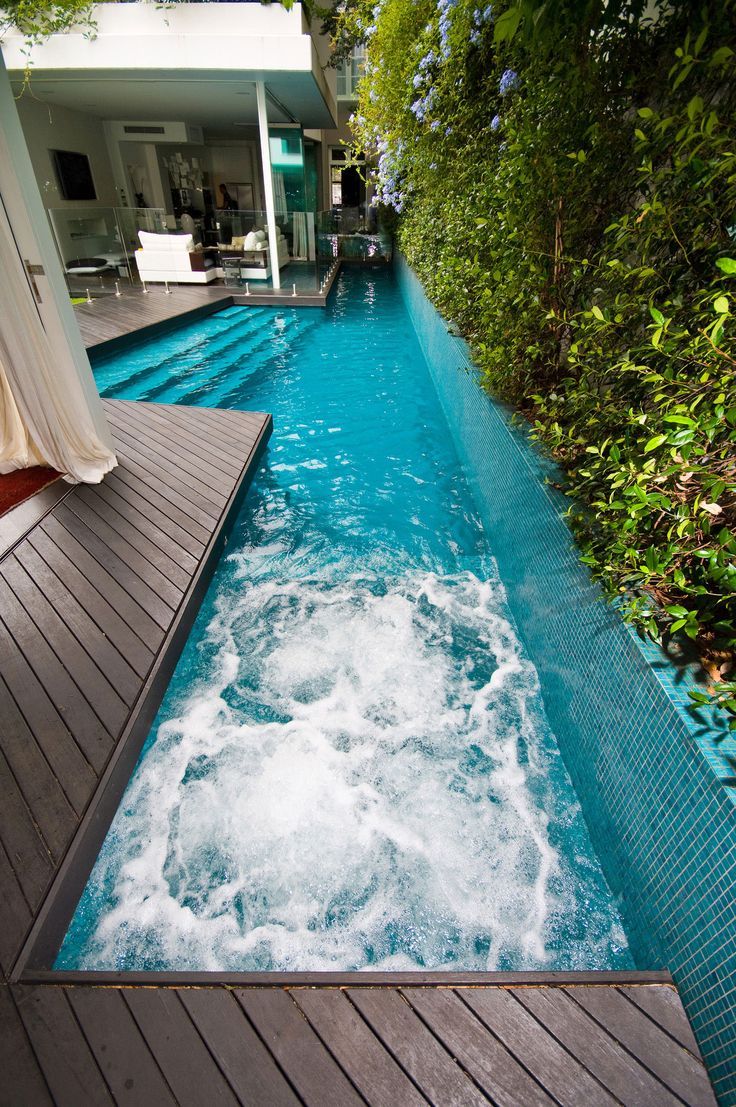 an outdoor swimming pool surrounded by greenery and wooden decking with water flowing down the side