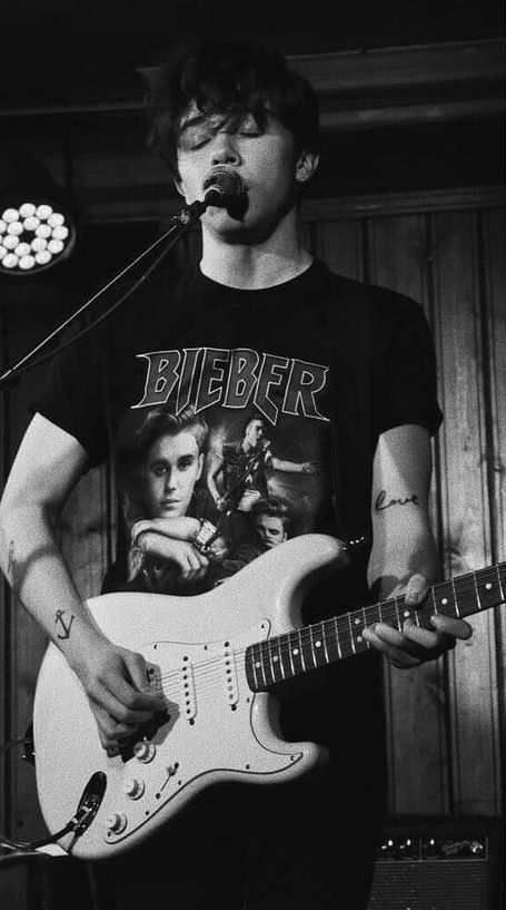 a young man is singing into a microphone while playing an electric guitar in front of him