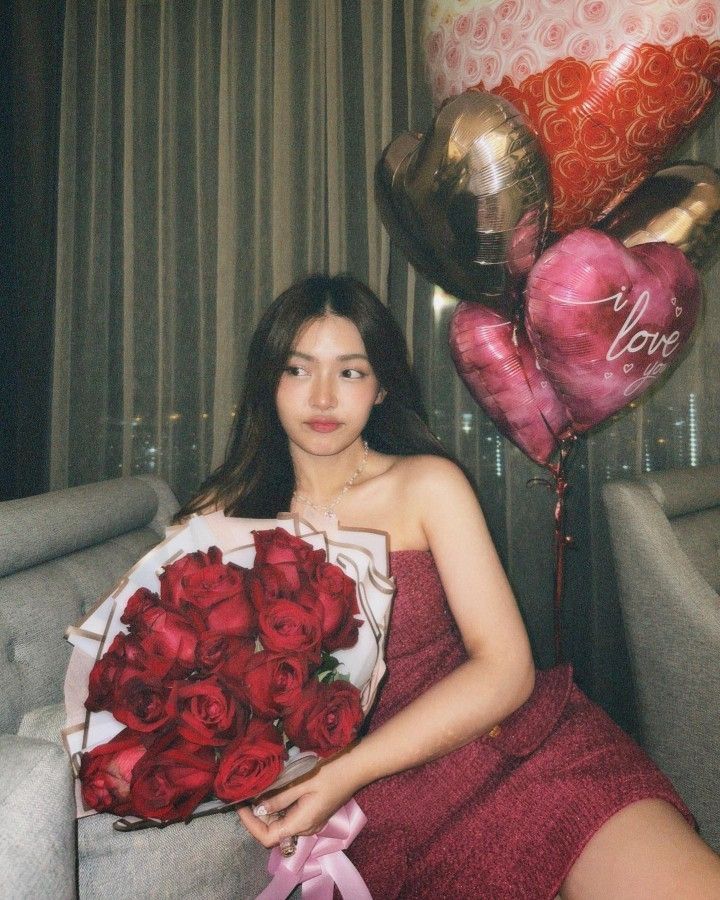 a woman sitting on a couch holding a bouquet of red roses and heart shaped balloons