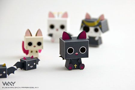 four small paper toy cats on a white surface with one black cat and one white cat