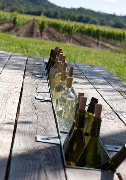 several bottles of wine are lined up on a picnic table in front of a vineyard