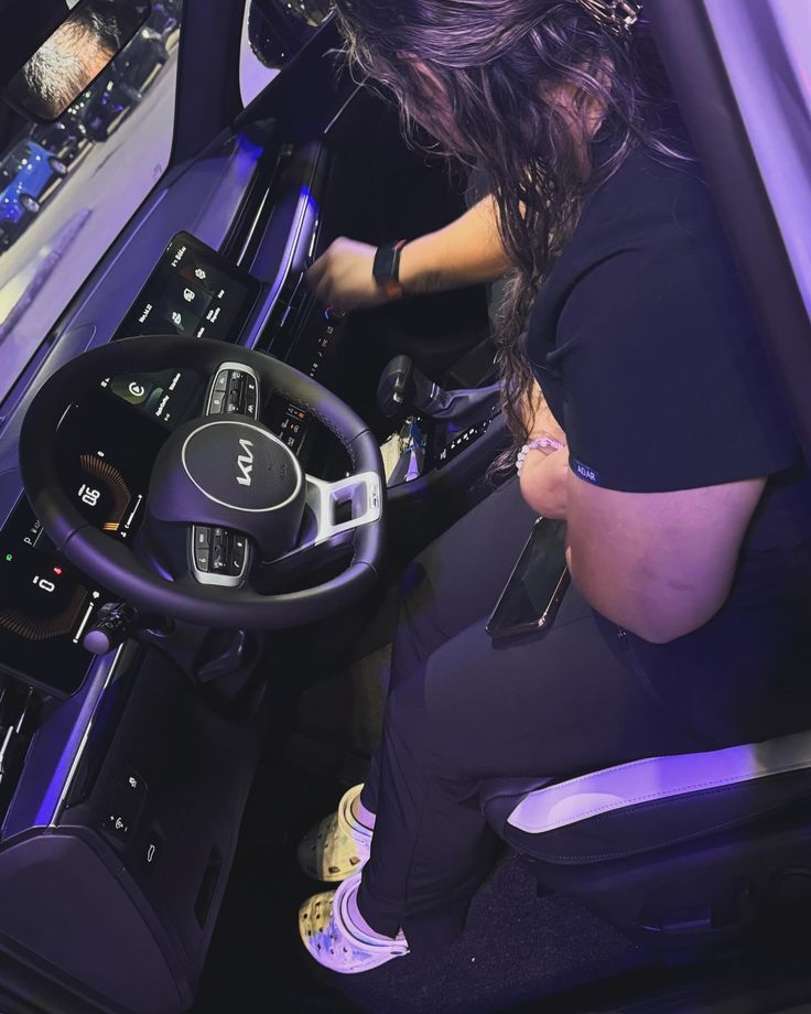 a woman sitting in the driver's seat of a car with her hands on the steering wheel