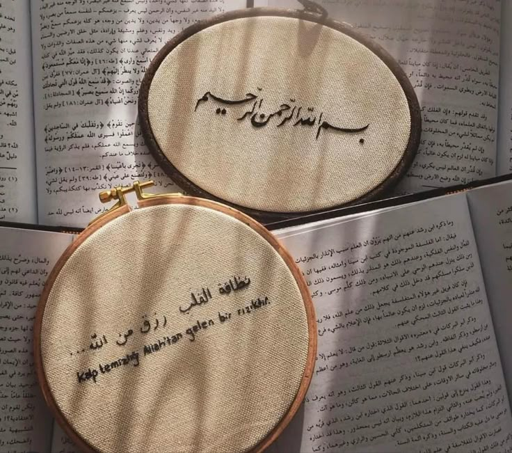 two embroidered hoops sitting on top of an open book with arabic writing in it