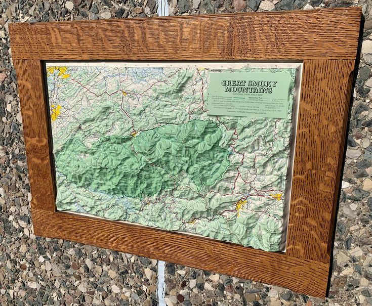 a wooden frame with a map hanging on it's side next to a rock wall