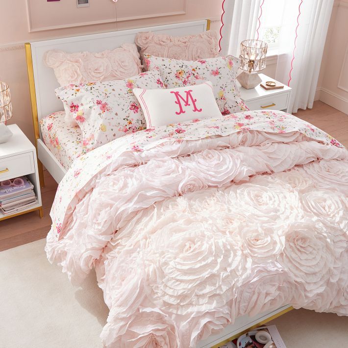 a bed with pink comforter and pillows in a bedroom next to a white nightstand