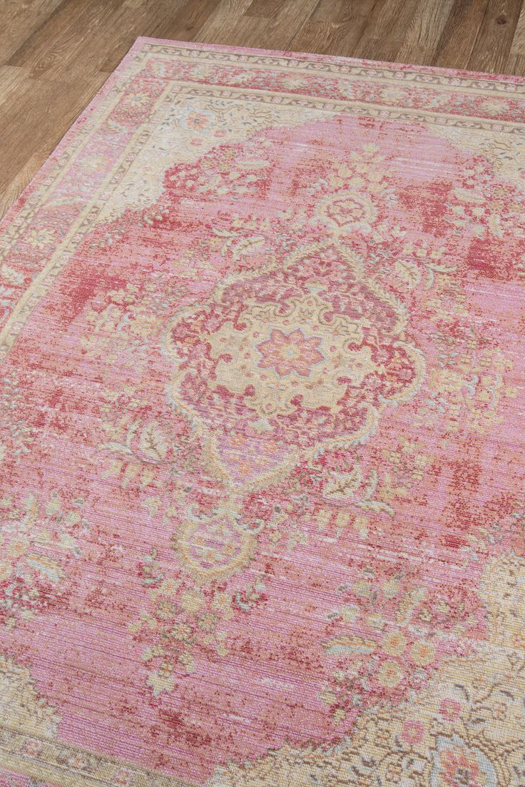 a pink and beige area rug with an ornate design on the center, surrounded by wood flooring