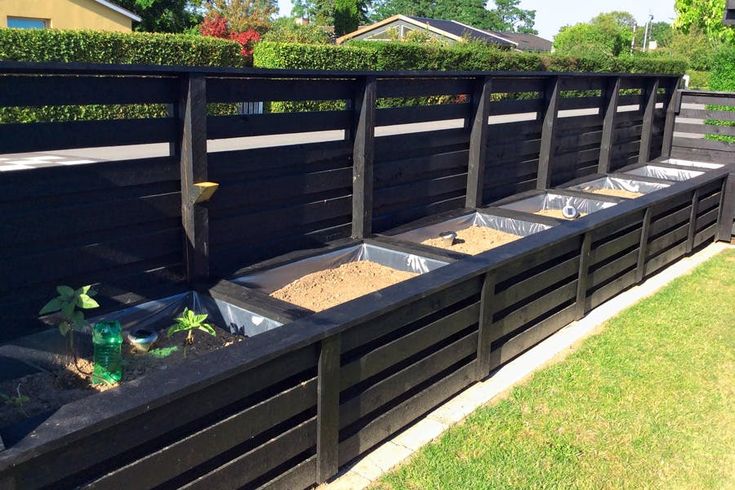 a row of black wooden planters filled with dirt and sand in the middle of a yard