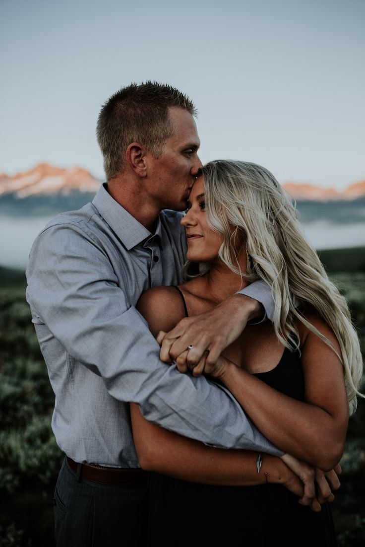 a man and woman embracing each other in the middle of a field with mountains in the background