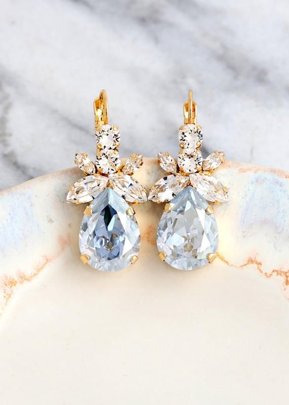 two pairs of gold and crystal earrings on a marble plate with white marble countertop