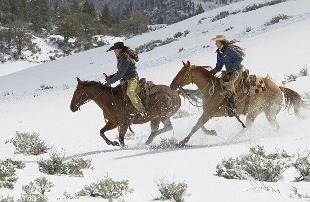 two women are riding horses in the snow