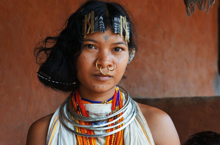 a woman wearing an elaborate necklace and nose ring with piercings on her head, standing in front of a wall