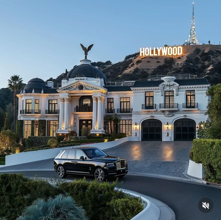 a black car is parked in front of a large white building with the hollywood sign above it