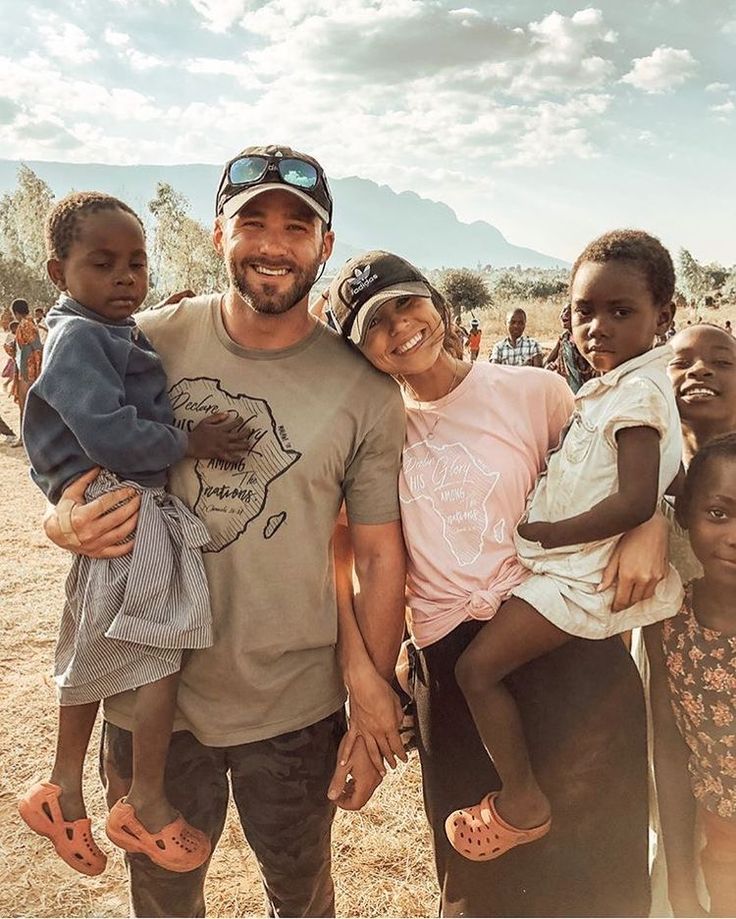 a man standing next to two children in front of a group of people on a dirt field