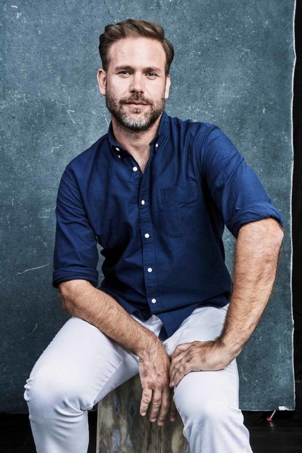 a man sitting on top of a wooden bench wearing white pants and a blue shirt