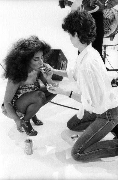 two women sitting on the floor eating food and talking to each other in front of a camera