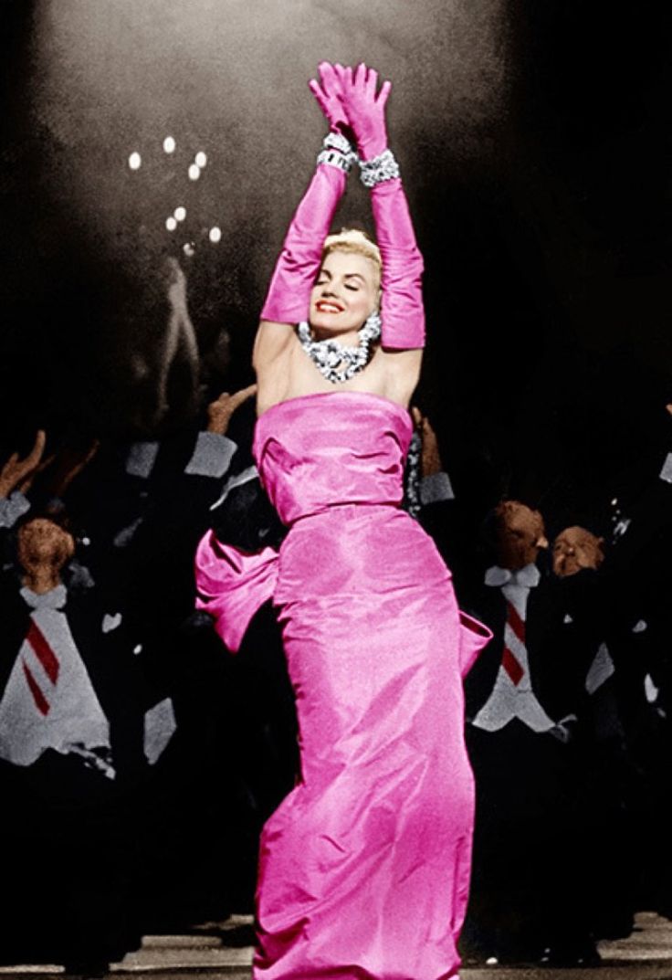 a woman in a pink dress is dancing with her hands up and other people behind her