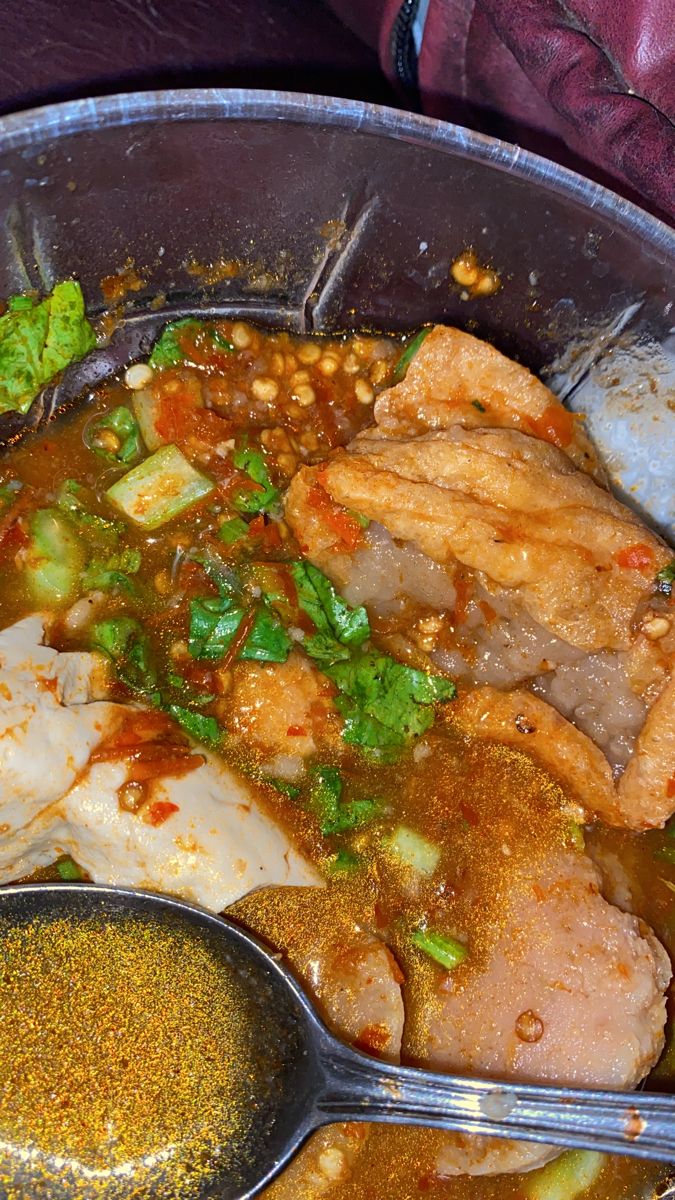 a metal bowl filled with meat and vegetables next to some seasoning on the side