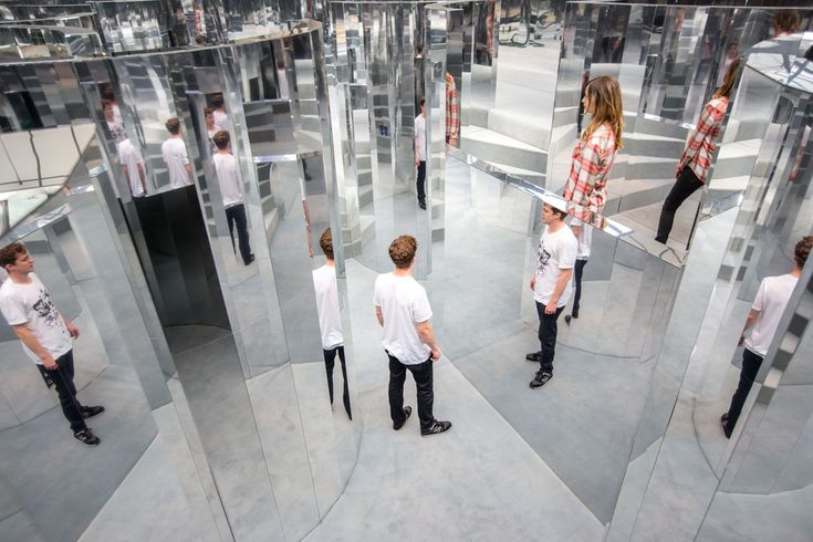 a group of people standing in front of mirrored walls with mirrors on the wall and one person looking at them