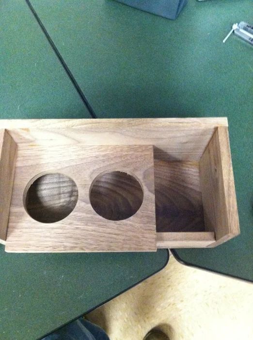 a wooden box with three holes in it on a table next to a person's feet