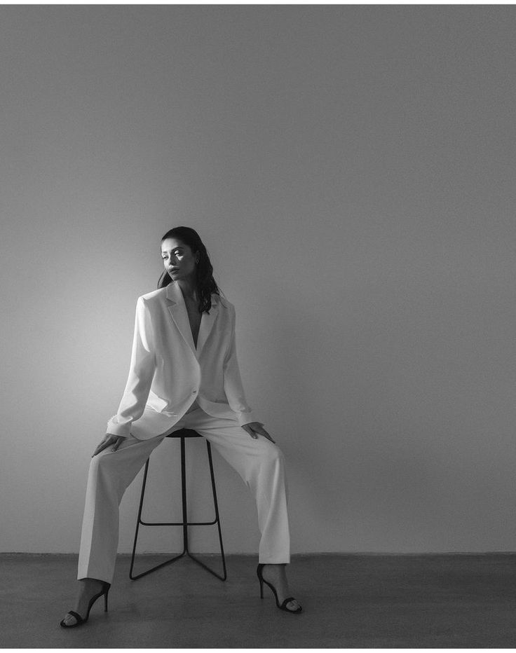 a woman sitting on top of a stool wearing a white suit and high heels with her legs crossed