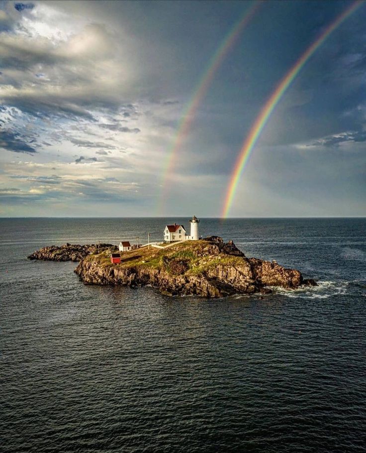 a rainbow is seen over an island in the middle of the ocean with lighthouses on it