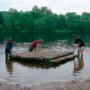 three people are standing on a raft in the water, and one person is cleaning it