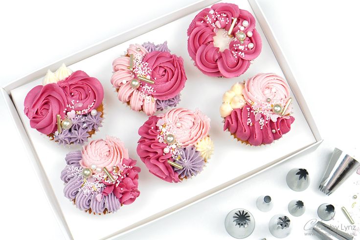 cupcakes decorated with pink and purple icing in a box next to other decorations