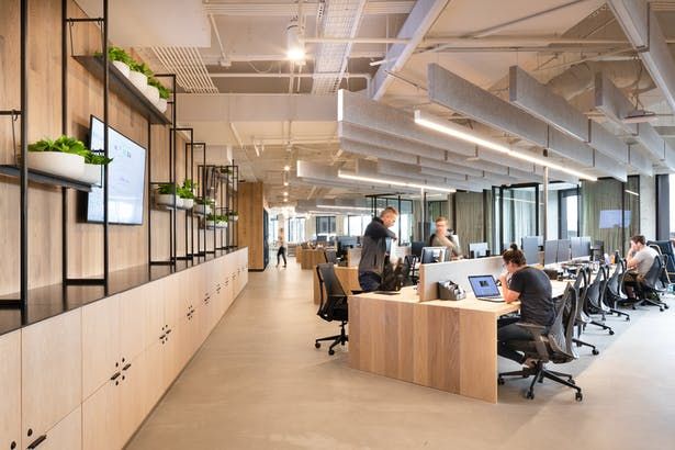 an office with people working on their computers and sitting at desks in front of large windows