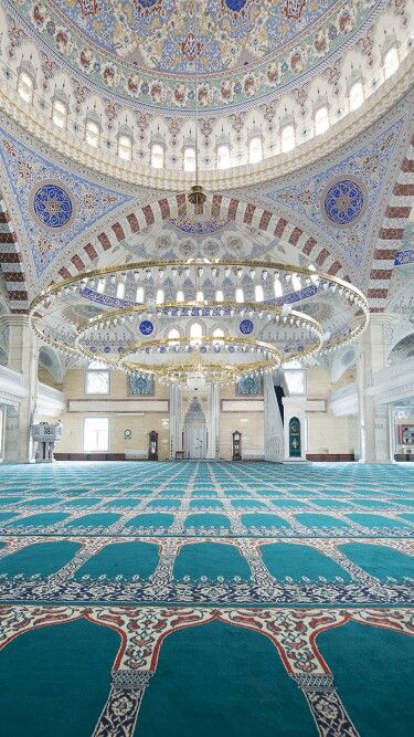 the interior of a mosque with an ornate ceiling and carpeted floor, with arabic writing on