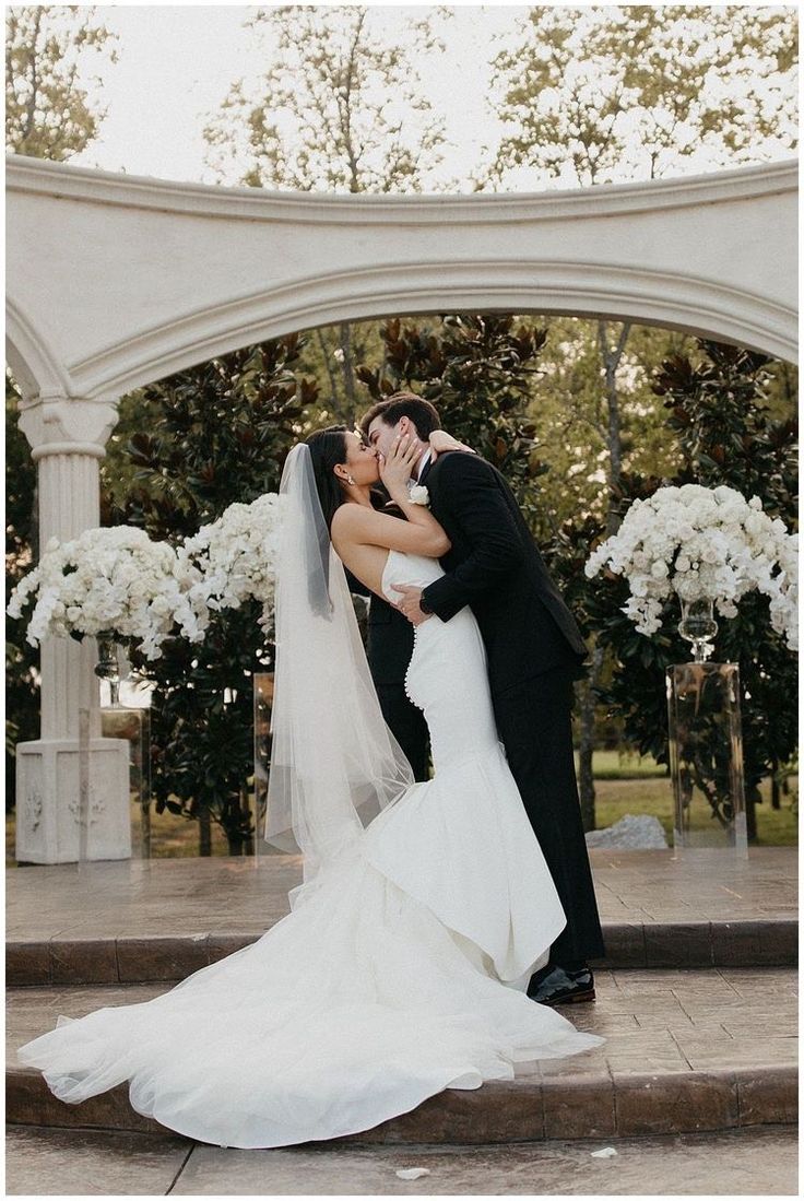 a bride and groom kissing in front of an arch with white flowers on the side