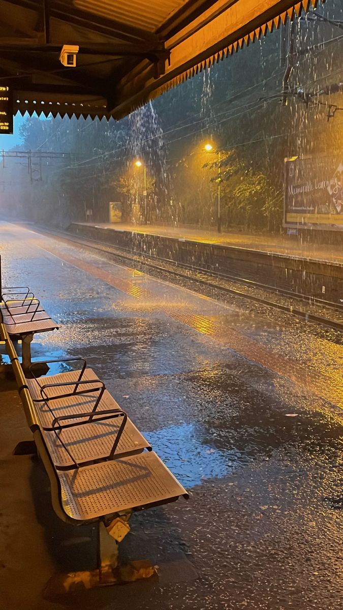 the rain is pouring down on benches at the train station