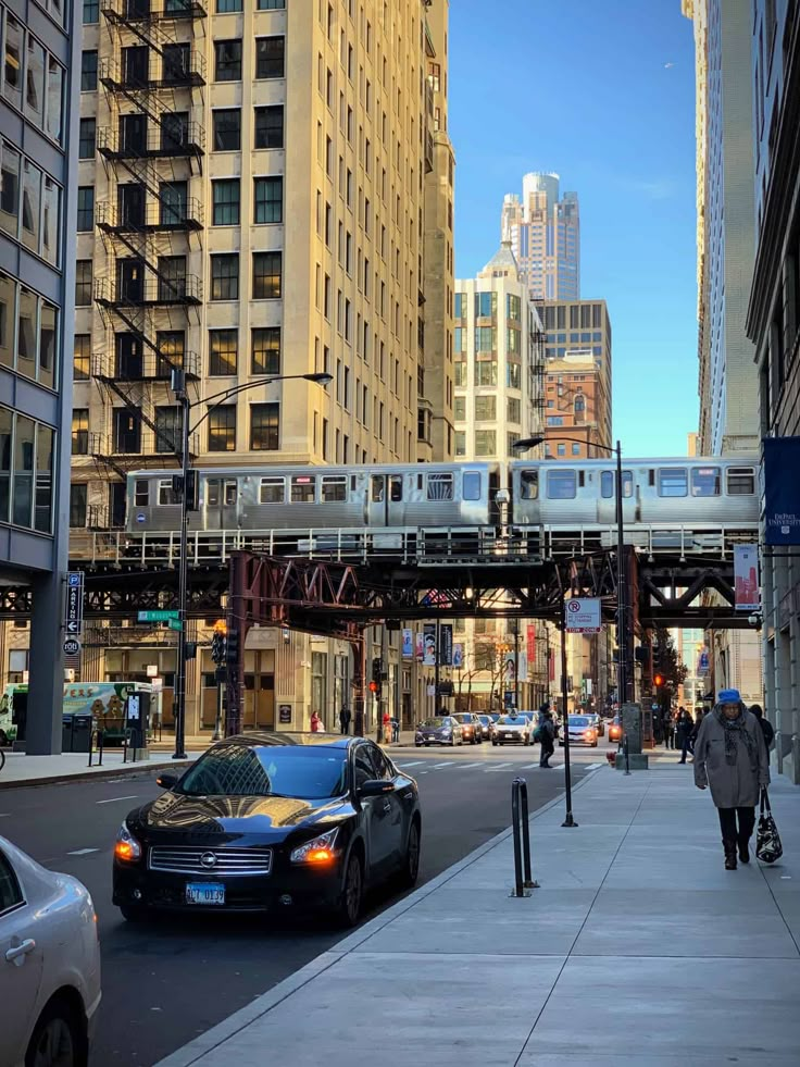 a city street with cars, people and a train on the tracks in the distance