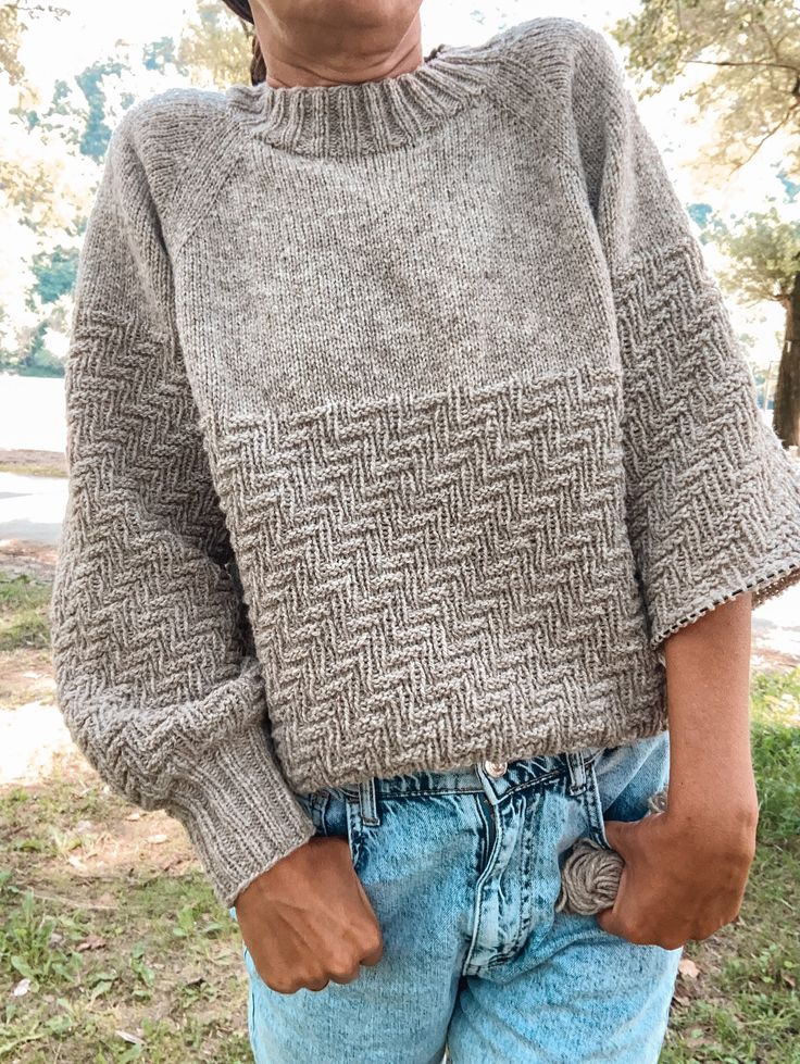 a woman wearing a gray sweater and denim shorts with her hands in her pockets while standing on the grass