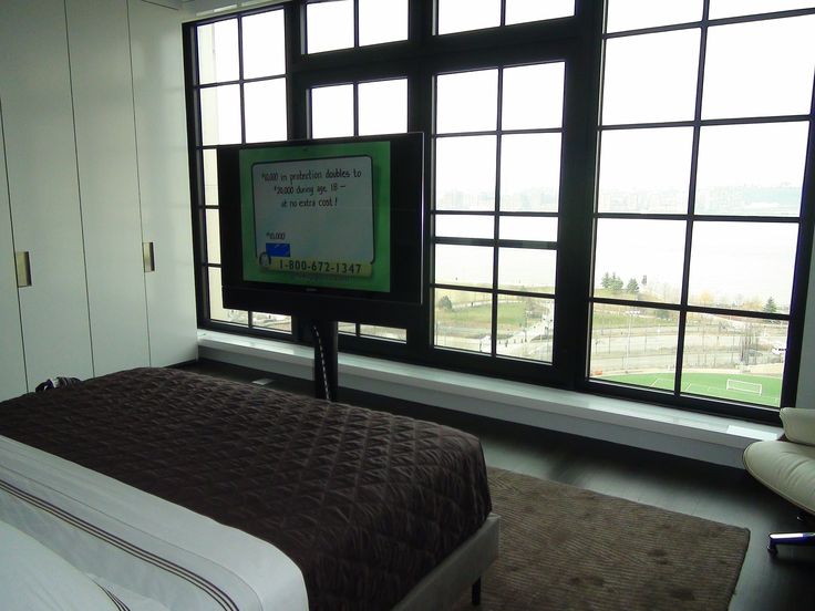 a bed sitting in front of a large window with a tv on top of it