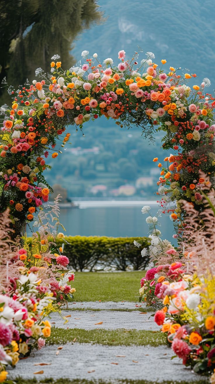 an arch made out of flowers on the side of a road with water in the background